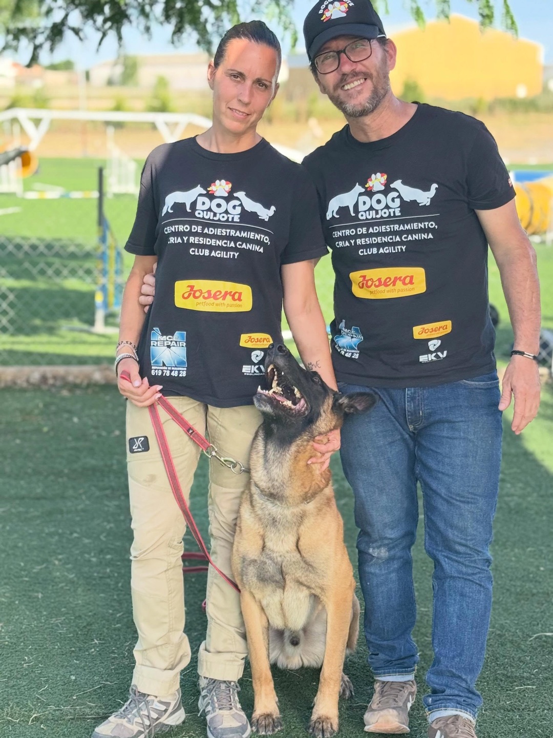 Dos adiestradores del club Dogquijote con camiseta del centro junto a un malinois en la pista